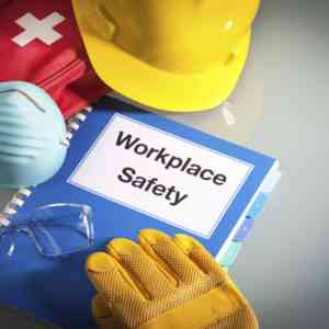 Workplace Safety Handbook with OSHA Requirements next to A First Aid Kit, Respirator Face Piece, Hart Hat, and Safety Gloves